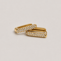 A pair of gold huggie hoop earrings with pavé-set clear stones, arranged on a light beige background.