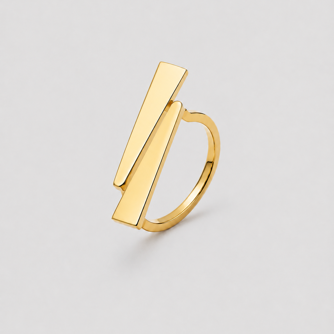 A gold geometric ring featuring two parallel rectangular bar elements set into a smooth band, photographed on a neutral light gray background.