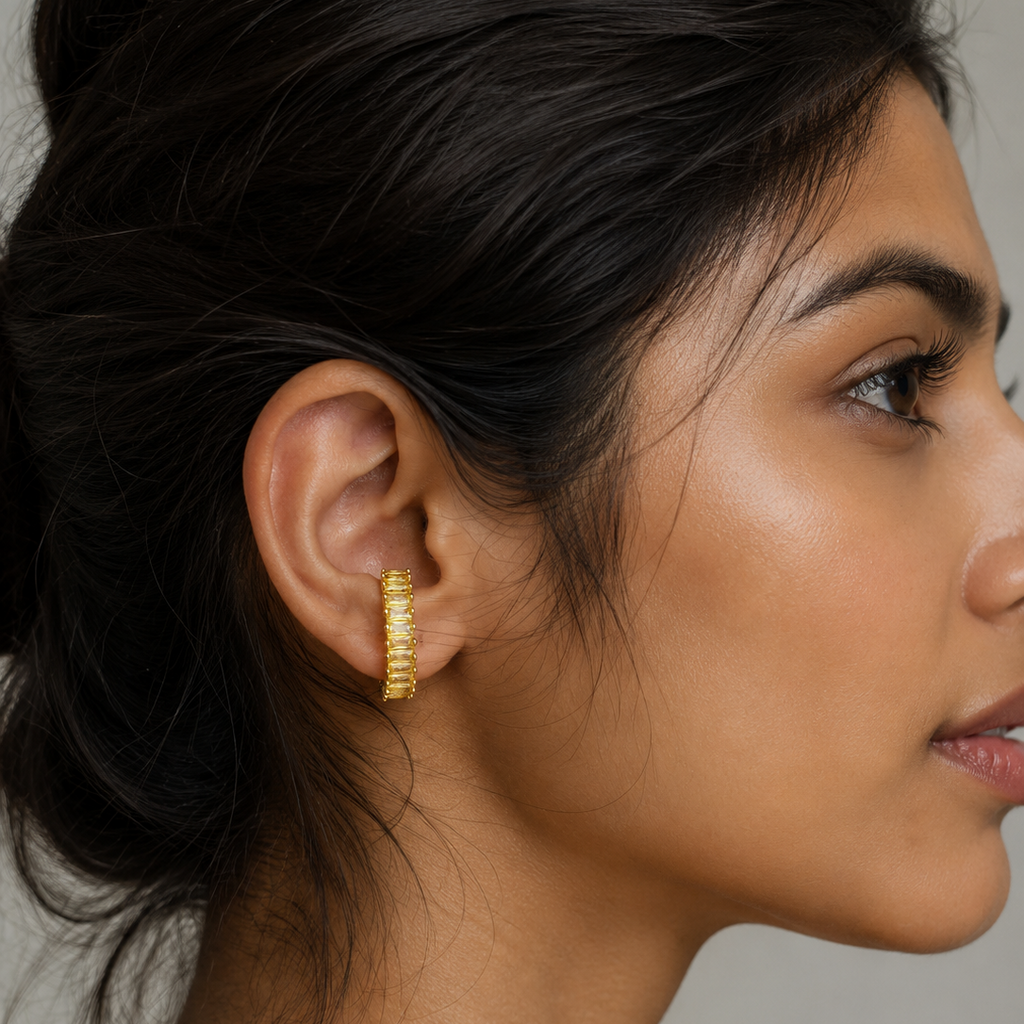 A close-up side profile of a woman wearing a small gold hoop earring with a textured, beaded or ridged design.
