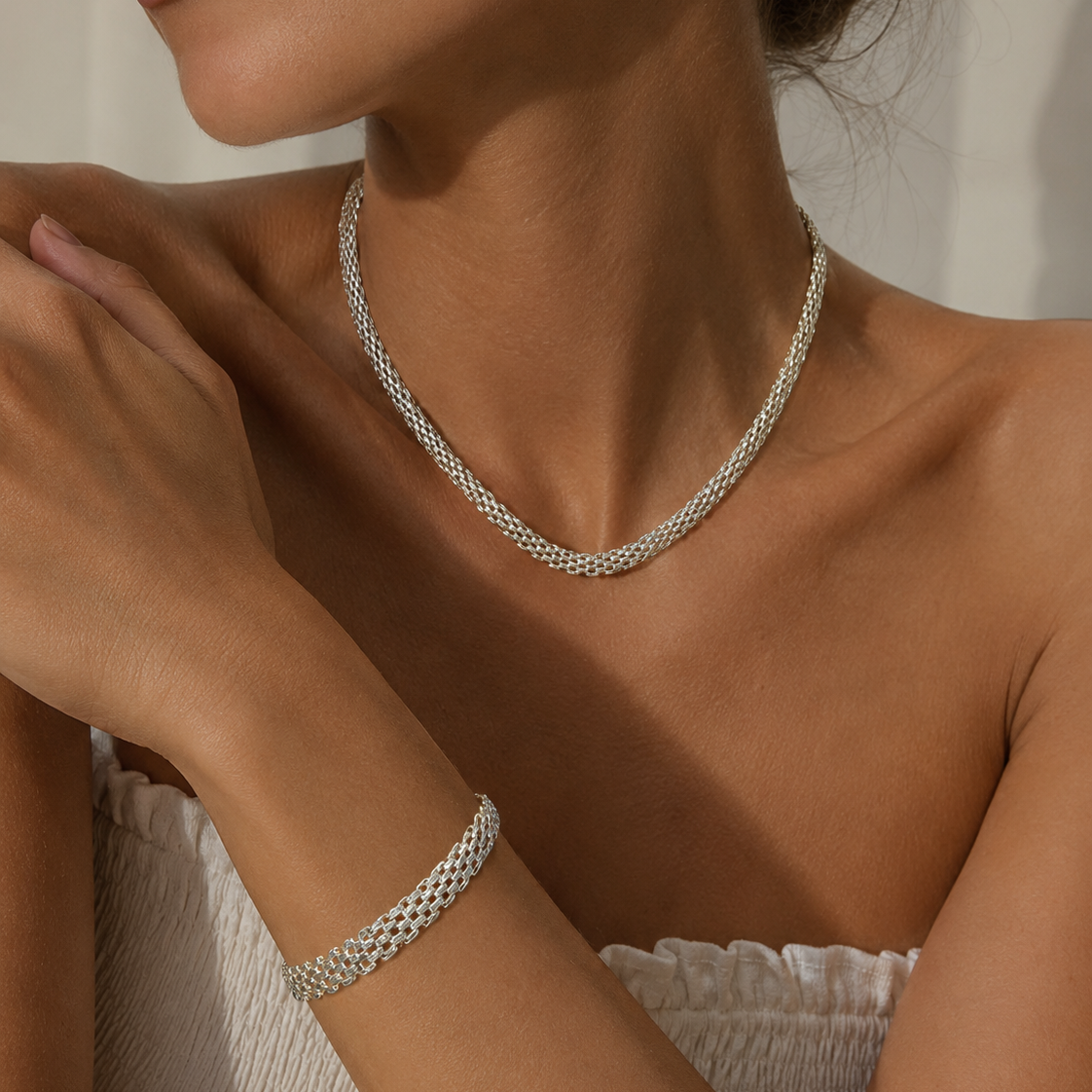 A close-up lifestyle shot of a model wearing a silver woven chain necklace and a matching silver woven bracelet.
