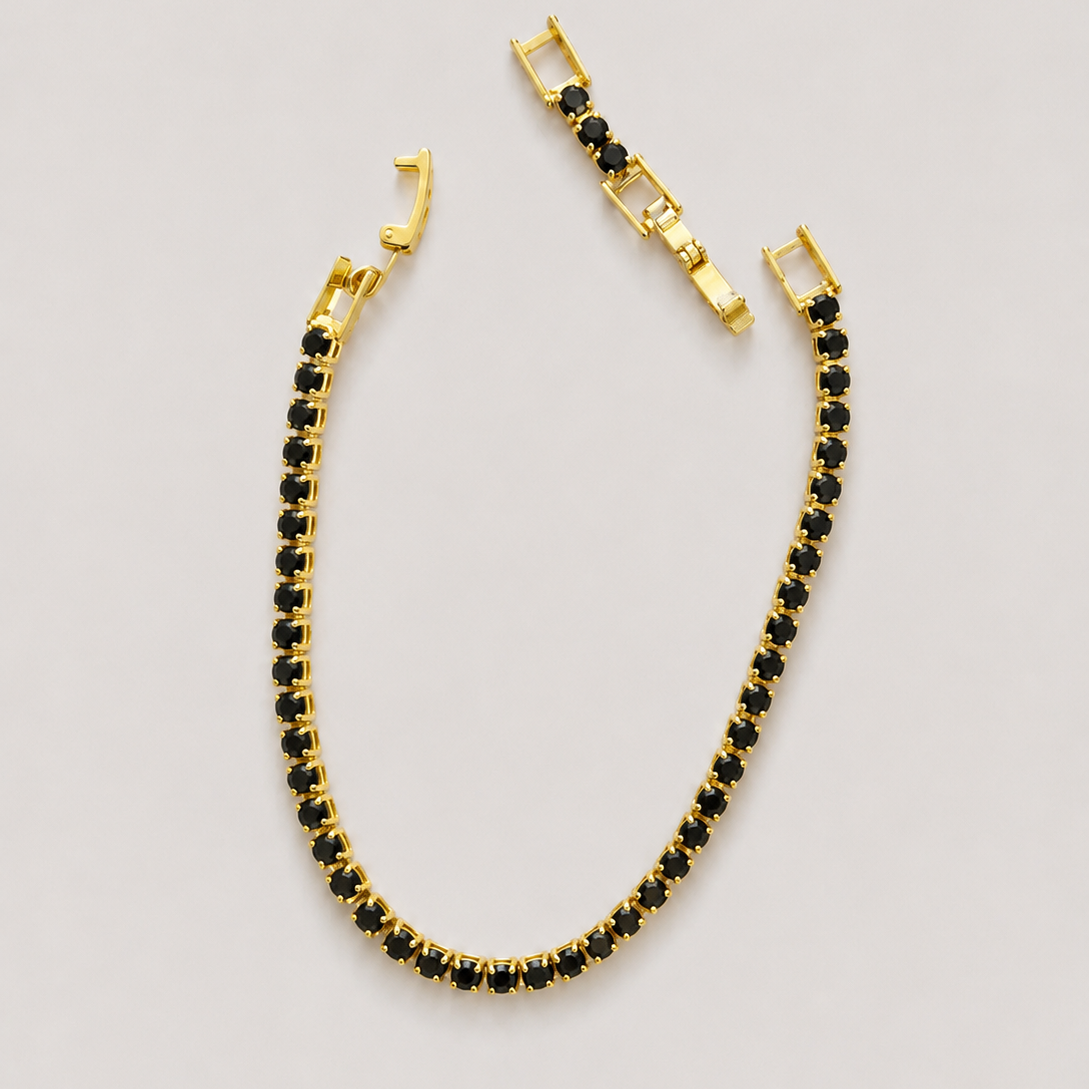 A gold tennis bracelet with small black stones, shown in a curved U-shape with its clasp detail displayed above it on a light gray background.