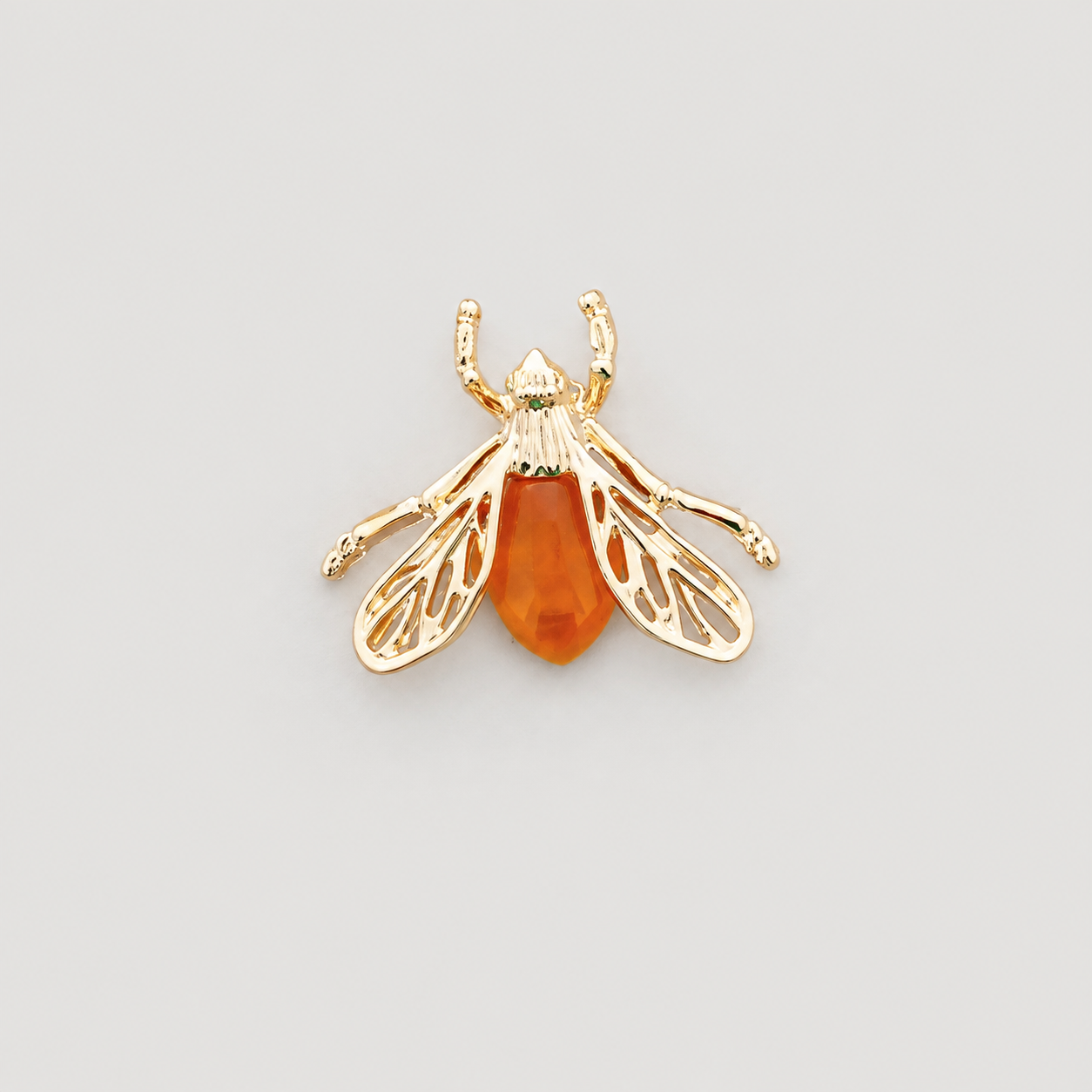 A gold bee-shaped brooch with a polished amber-orange body, photographed on a clean light gray background.