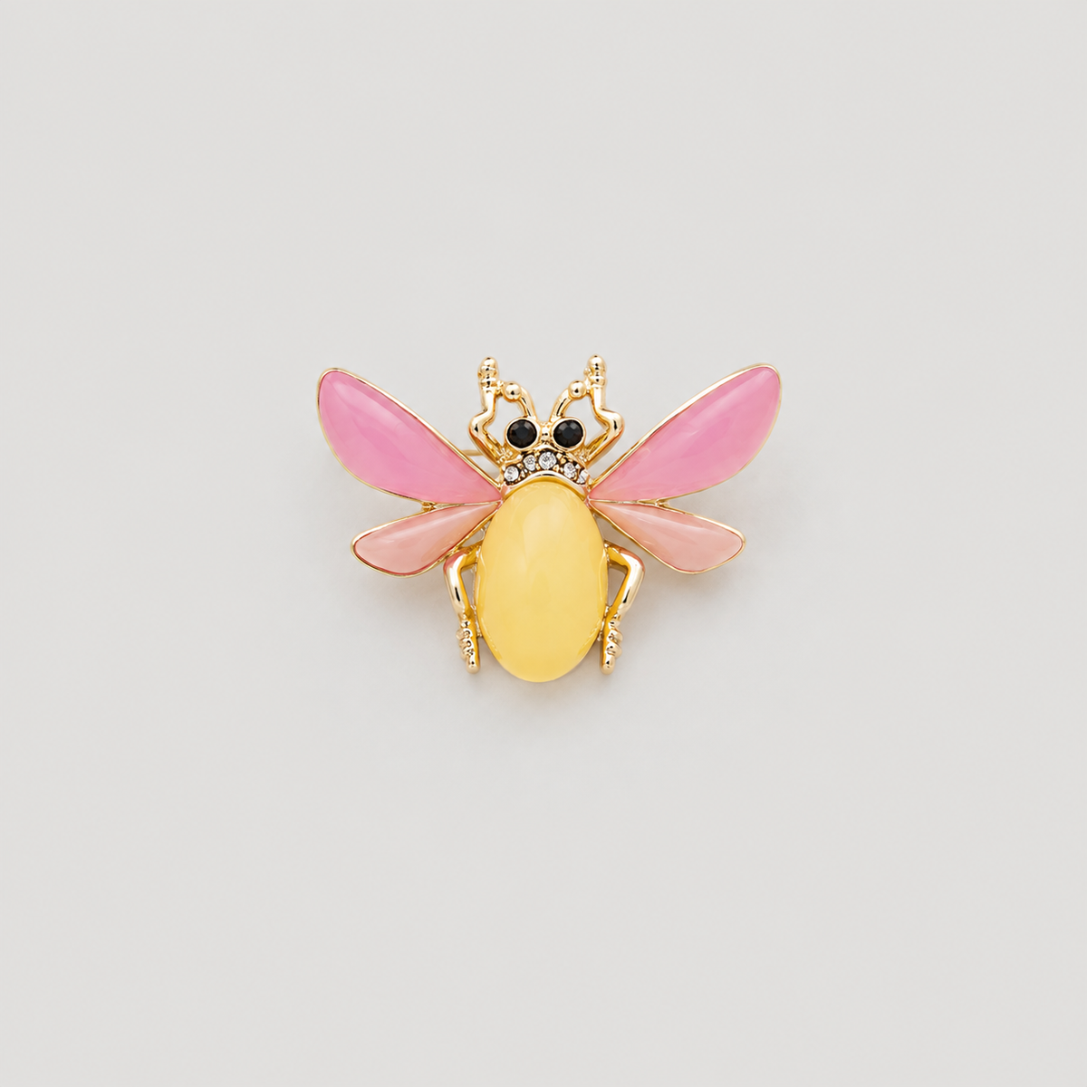 A gold-tone bee-shaped brooch with pink wings and a yellow body, centered on a light gray background.