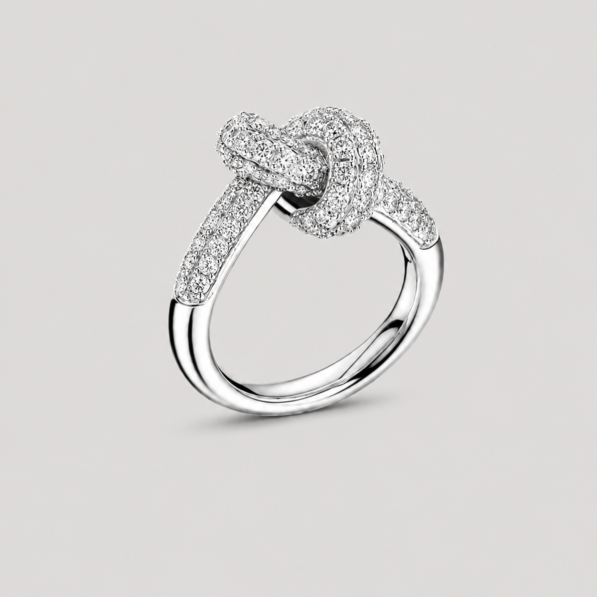 A silver knot ring with pavé-set clear stones, shown on a neutral light gray background.