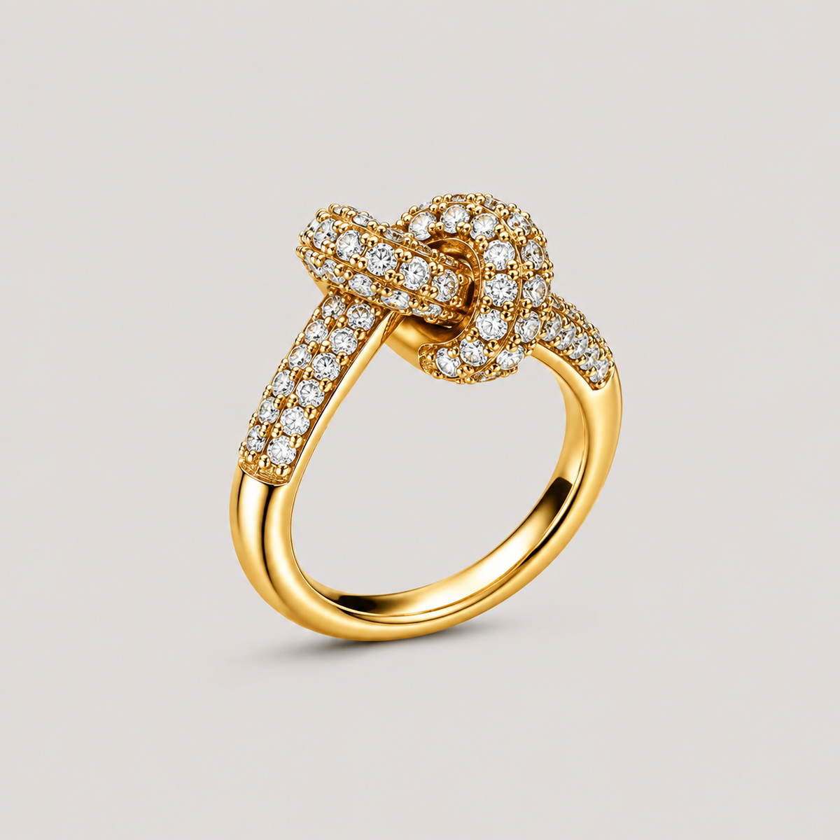 A gold ring featuring a knotted bow design paved with small clear stones, set against a solid light gray background.