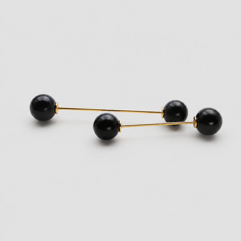 A pair of gold-toned double-bar earrings with four black spherical beads, arranged diagonally on a light gray background.