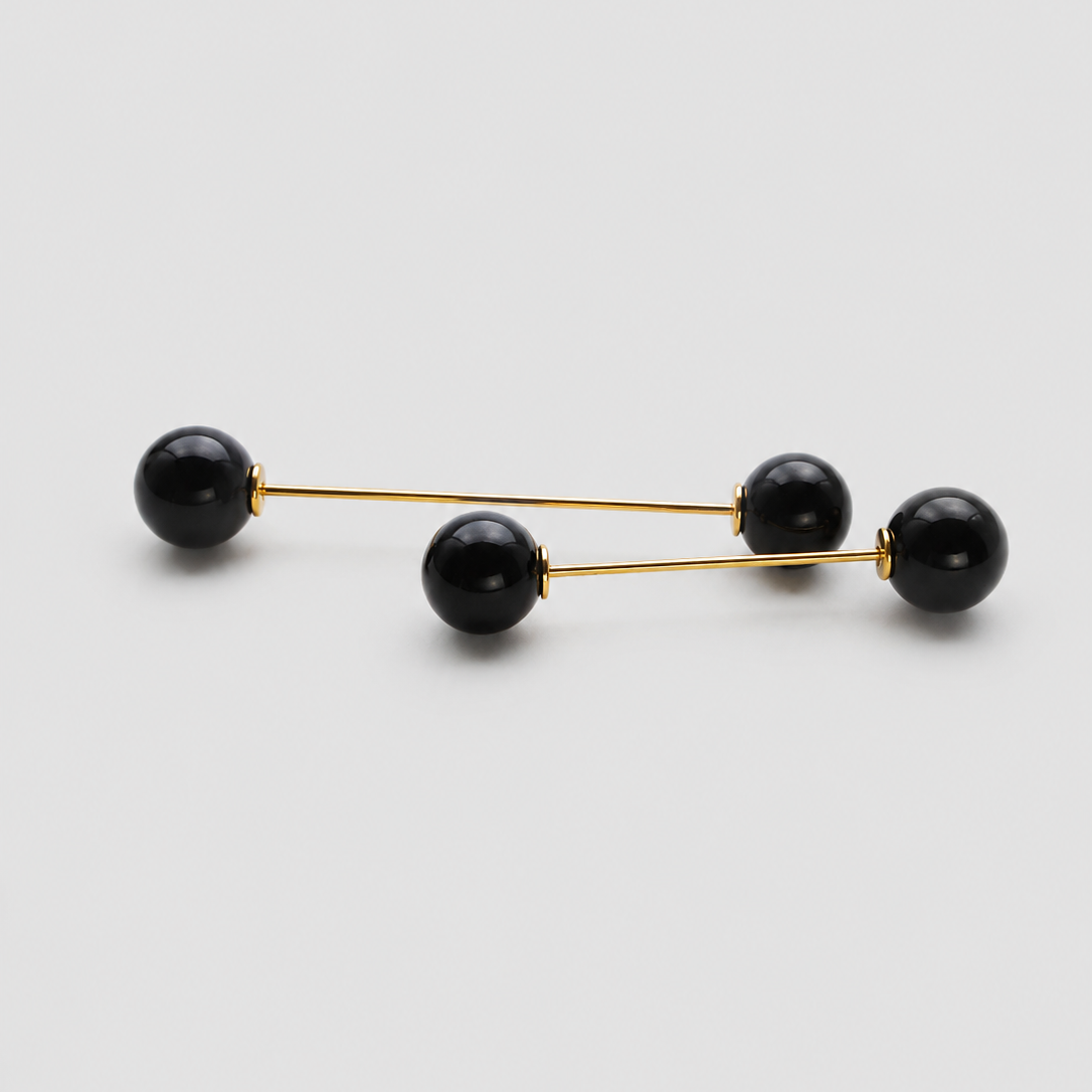 A pair of gold-toned double-bar earrings with four black spherical beads, arranged diagonally on a light gray background.