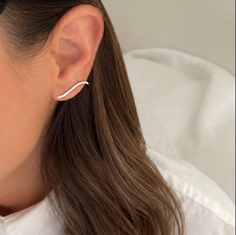 A close-up of a woman wearing a black baseball cap with a small black embroidered New Era logo on the side, a white collared shirt, and a delicate silver C-shaped ear cuff.