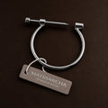 A silver-toned metal cuff bracelet with a sliding screw closure, shown on a dark brown textured background with a branded hangtag reading Matriarcha.