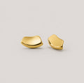 A pair of abstract, organic-shaped gold stud earrings on a light gray background.