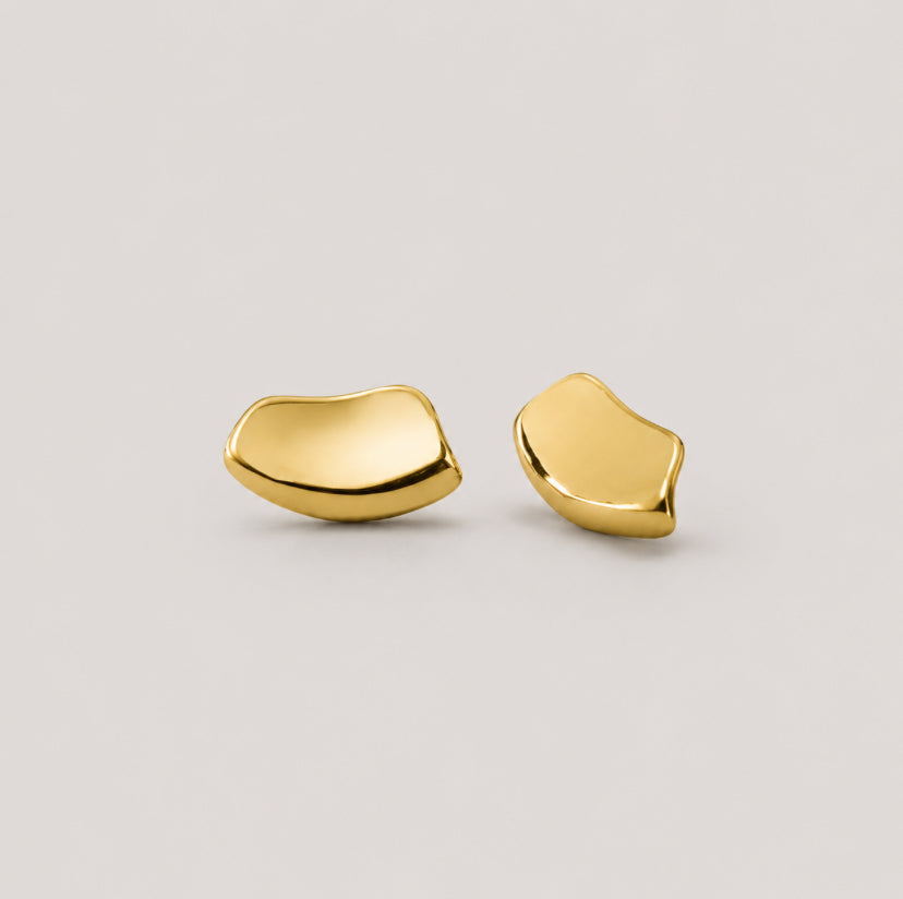 A pair of abstract, organic-shaped gold stud earrings on a light gray background.