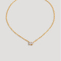 A delicate gold chain necklace with a small central gold bow-shaped setting holding a clear gemstone, displayed against a solid light gray background.