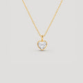A delicate gold chain necklace with a small heart-shaped pendant set with a clear heart-shaped gemstone, displayed against a solid light gray background.