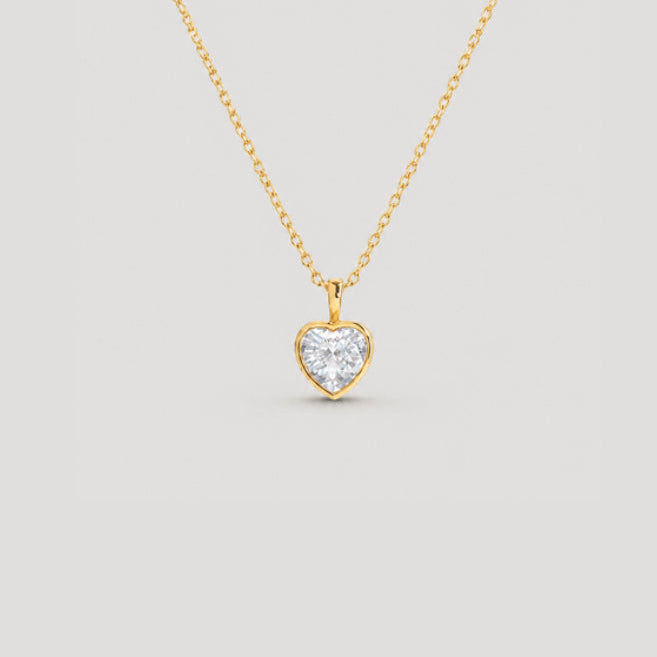 A delicate gold chain necklace with a small heart-shaped pendant set with a clear heart-shaped gemstone, displayed against a solid light gray background.