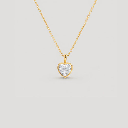 A delicate gold chain necklace with a small heart-shaped pendant set with a clear heart-shaped gemstone, displayed against a solid light gray background.