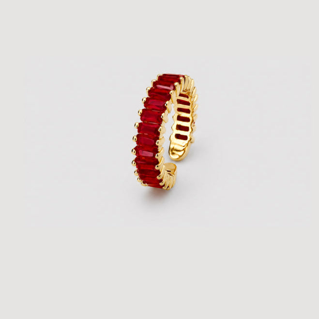A gold-plated cuff ring featuring a single row of rectangular red gemstones, shown on a neutral light gray background.