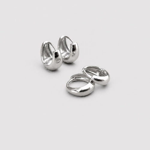 A pair of polished silver huggie hoop earrings shown on a clean, light gray background.
