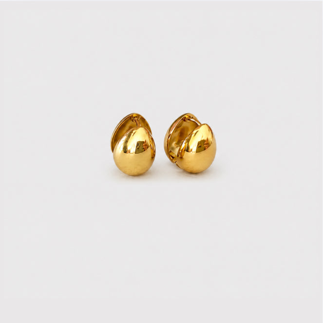 A pair of small, polished gold stud earrings shaped like stylized teardrops or leaves, displayed on a clean, light gray background.