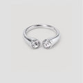 A silver-toned split ring featuring two bezel-set clear round gemstones, shown against a neutral light gray background.