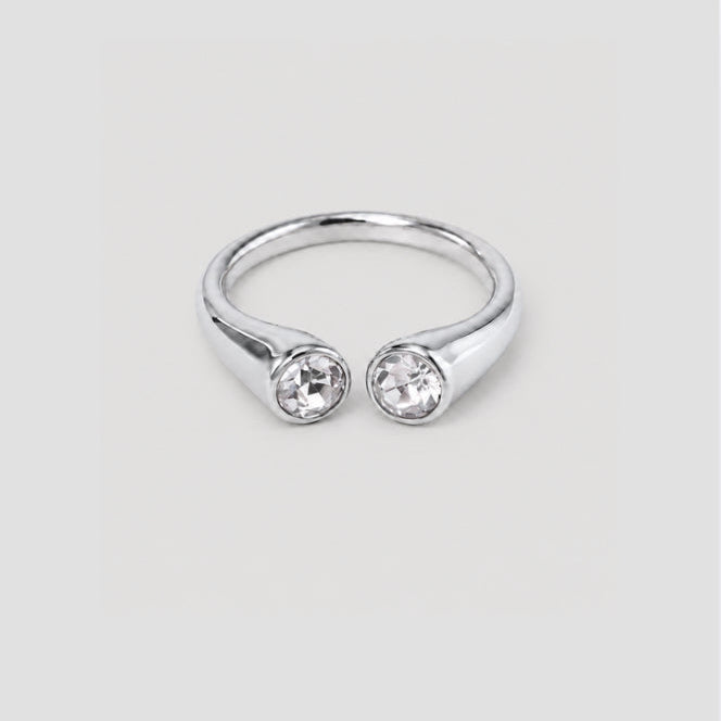 A silver-toned split ring featuring two bezel-set clear round gemstones, shown against a neutral light gray background.