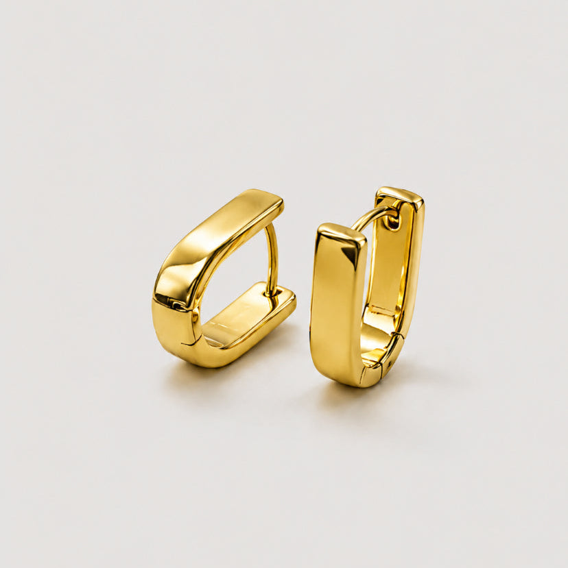 A pair of polished gold huggie hoop earrings with a modern, slightly angled rectangular design, displayed on a clean light gray background.