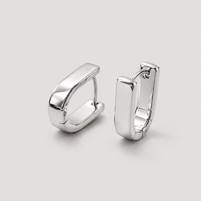 A pair of polished silver huggie hoop earrings with a modern, chunky rectangular design, displayed on a neutral light gray background.