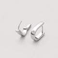 A pair of polished silver u shaped huggie hoop earrings on a light gray background.