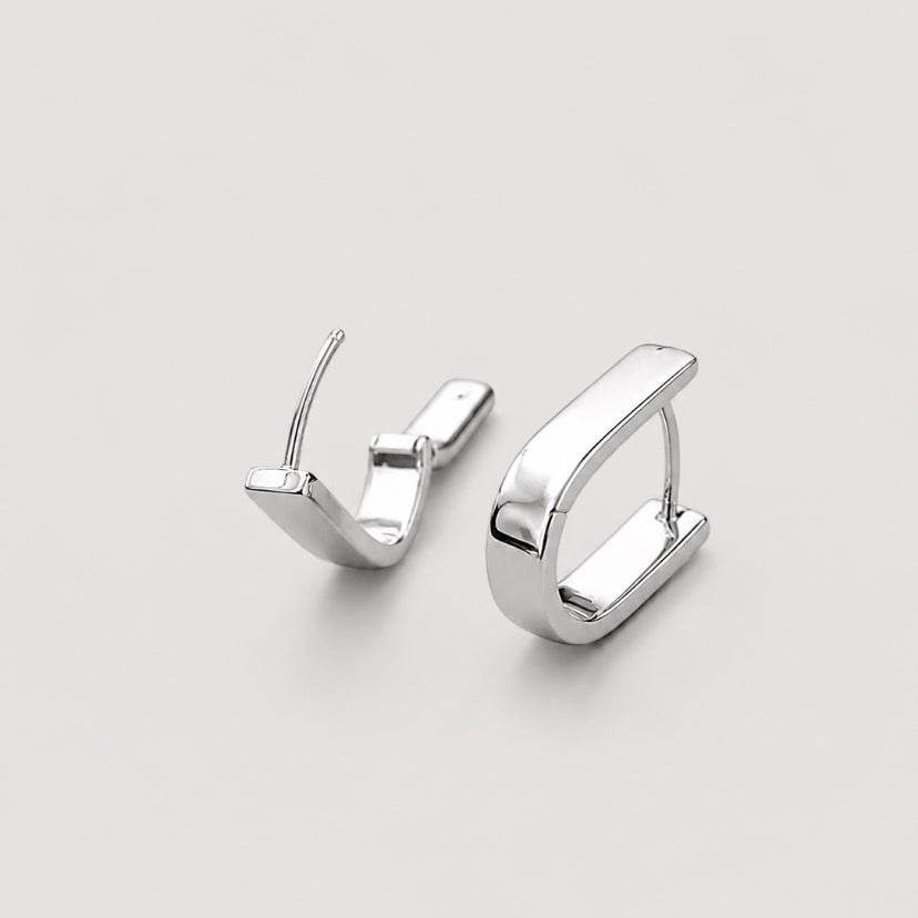 A pair of polished silver u shaped huggie hoop earrings on a light gray background.