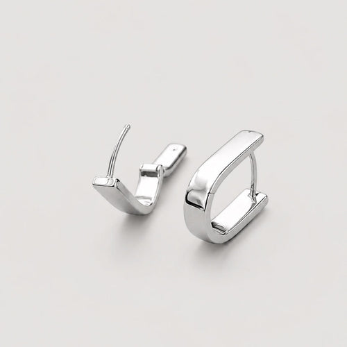 A pair of polished silver u shaped huggie hoop earrings on a light gray background.