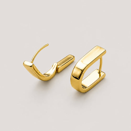 A pair of polished gold huggie with a round U shaped hoop earrings, displayed on a neutral light gray background.