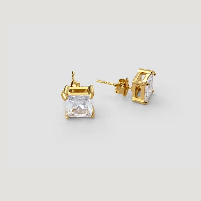 A pair of gold stud earrings with rectangular clear gemstones, shown on a light gray background.