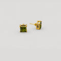 A pair of gold stud earrings with square-cut green gemstones, shown from both front and side angles on a light gray background.