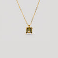 A gold chain necklace with a square-cut olive green gemstone pendant, displayed against a solid light gray background.