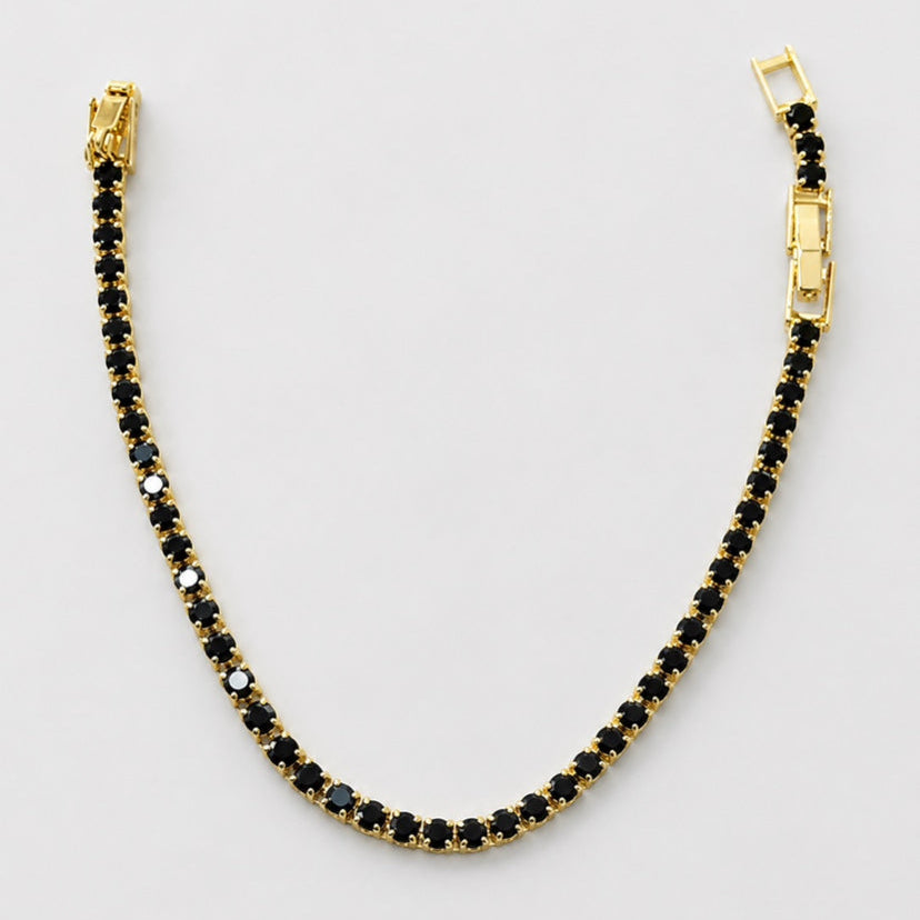 A gold tennis bracelet with small black stones, displayed in a curved shape on a light gray background.