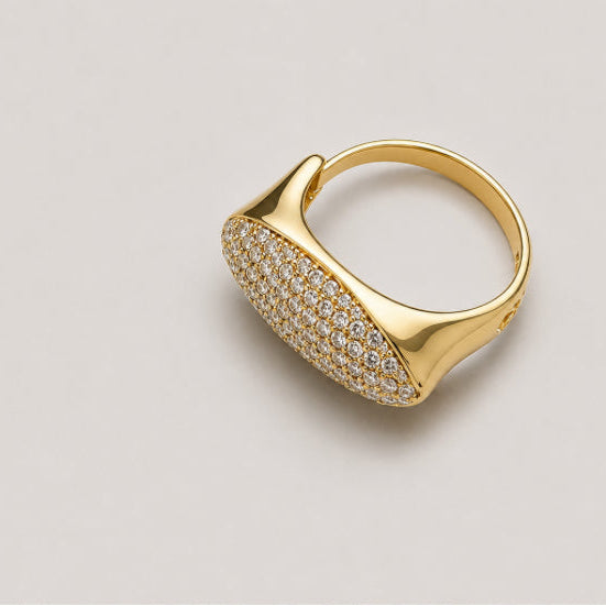A gold signet-style ring with a pavé-set oval face, photographed on a clean light gray background.
