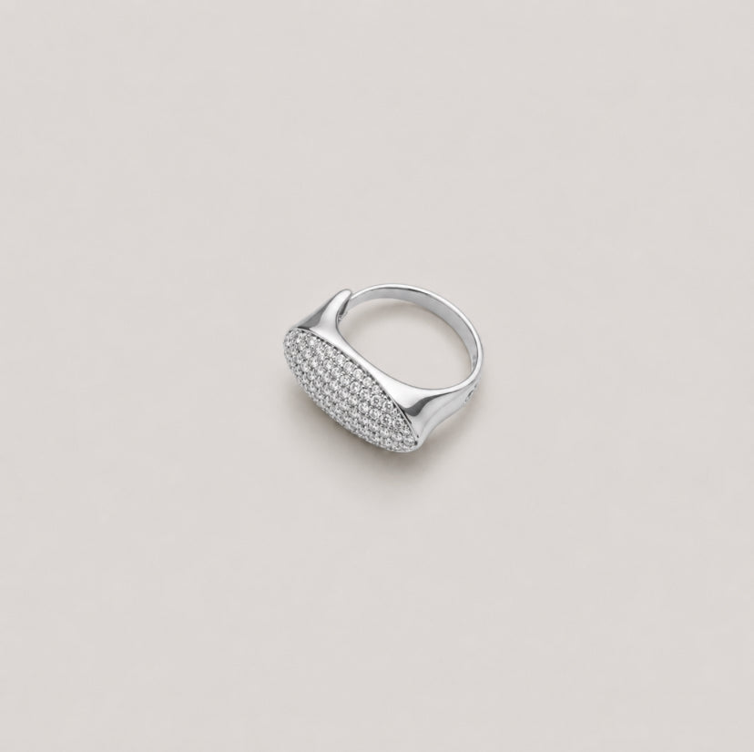 A silver signet ring with a textured pavé diamond face, photographed on a neutral light beige background.