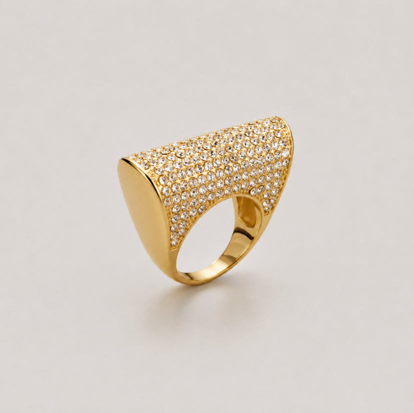 A gold ring with a wide, curved pavé-set top and a smooth polished band, photographed on a light gray background.