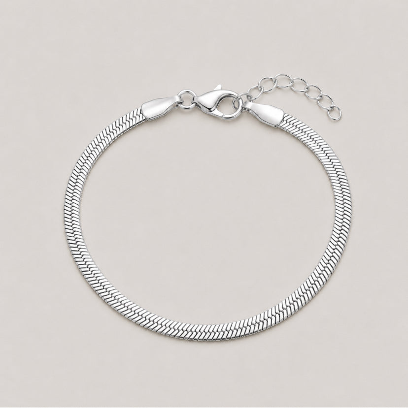 A silver snake chain bracelet with a lobster clasp and extension chain, displayed on a light beige background.