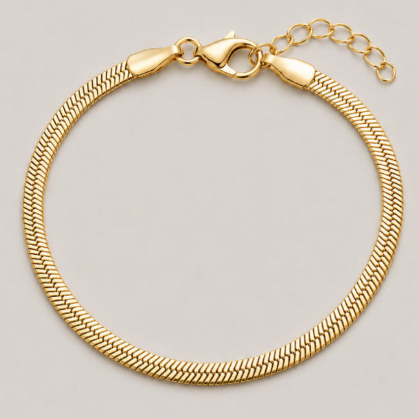 A gold-colored snake chain bracelet with a lobster clasp and extender chain, displayed on a neutral light gray background.