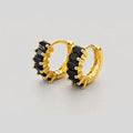 A pair of gold huggie hoop earrings with black crystal accents, displayed on a neutral light gray background.