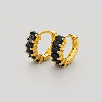 A pair of gold huggie hoop earrings with black crystal accents, displayed on a neutral light gray background.