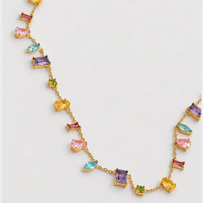 A gold chain necklace featuring multiple small rectangular and marquise-cut gemstones in pink, purple, blue, yellow, and green, arranged symmetrically on a light gray background.