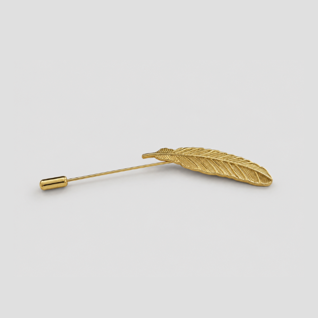 A gold feather pin with a textured feather head and a fine post, shown on a plain light gray background.