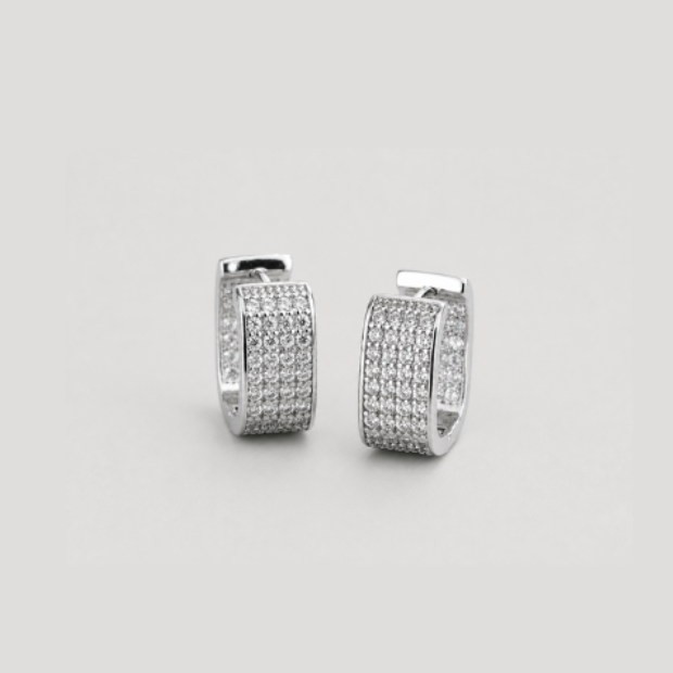 A pair of small silver huggie hoop earrings covered in clear pavé stones, centered on a solid light gray background.