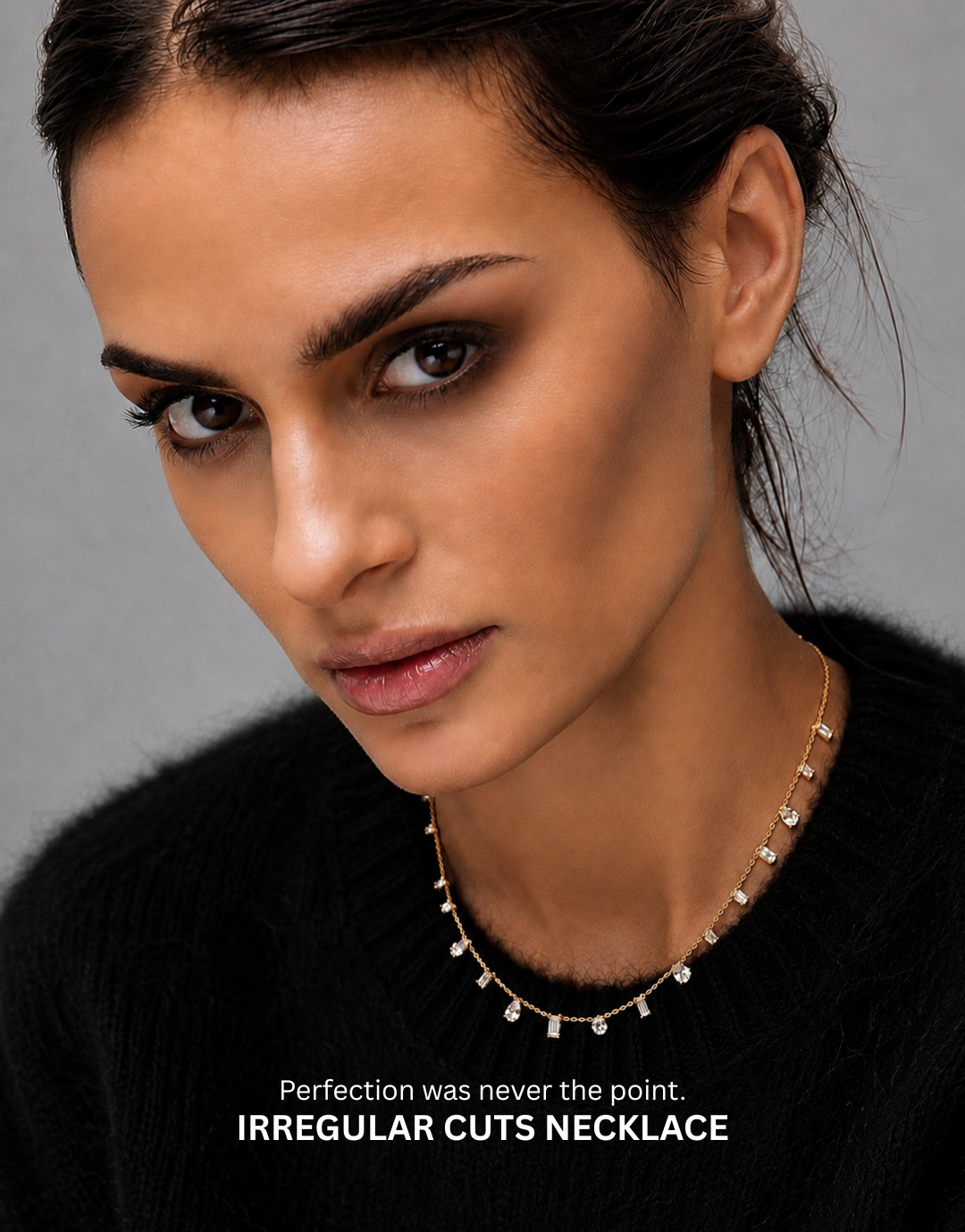 A close-up portrait of a woman wearing a delicate gold necklace with irregular-cut stones, set against a dark gray background. The bottom of the image features a black banner with white text that reads 'Perfection was never the point.